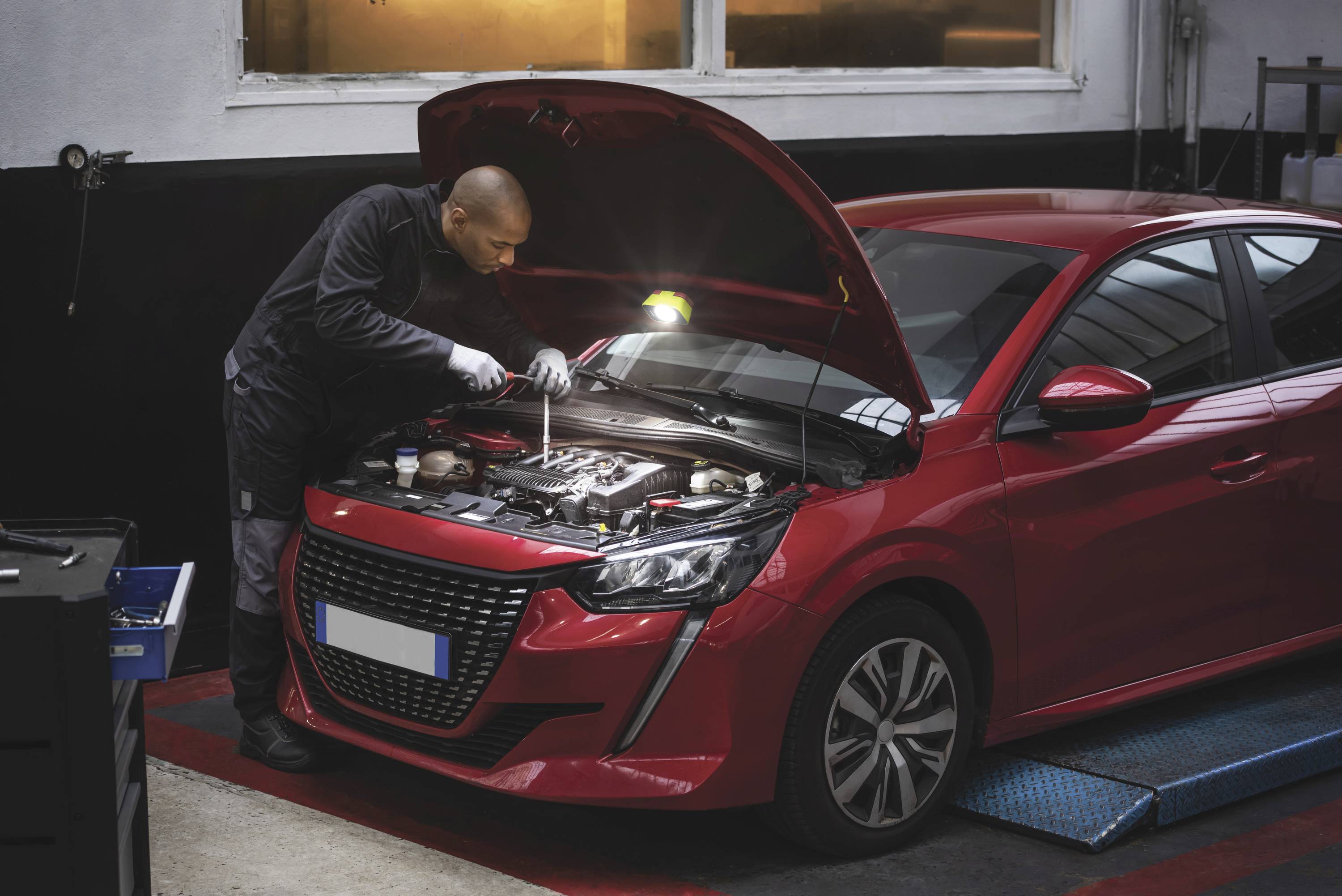 Un mécanicien répare une petite voiture rouge avec le capot ouvert dans un atelier automobile. Focus sur le moteur.