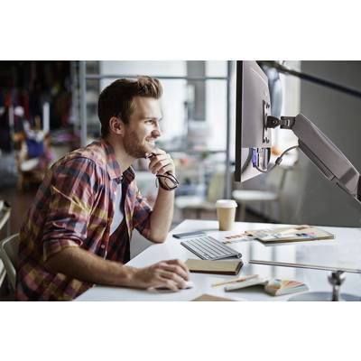 Un homme est assis souriant à un bureau devant un écran d'ordinateur, entouré de cahiers et de matériel de dessin.