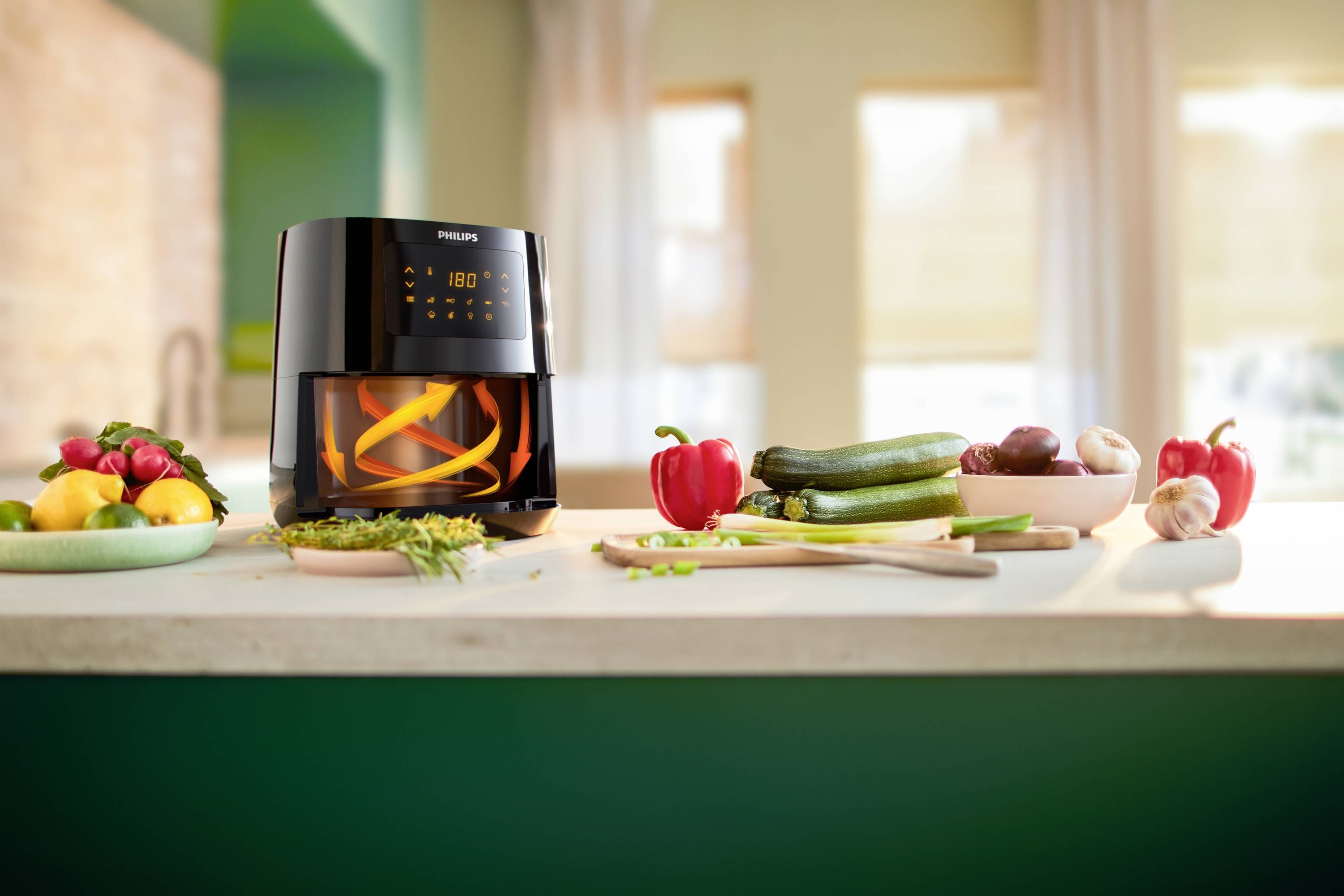 Un airfryer moderne est posé sur un plan de travail de cuisine, entouré de légumes frais tels que des poivrons, des courgettes et des oignons.