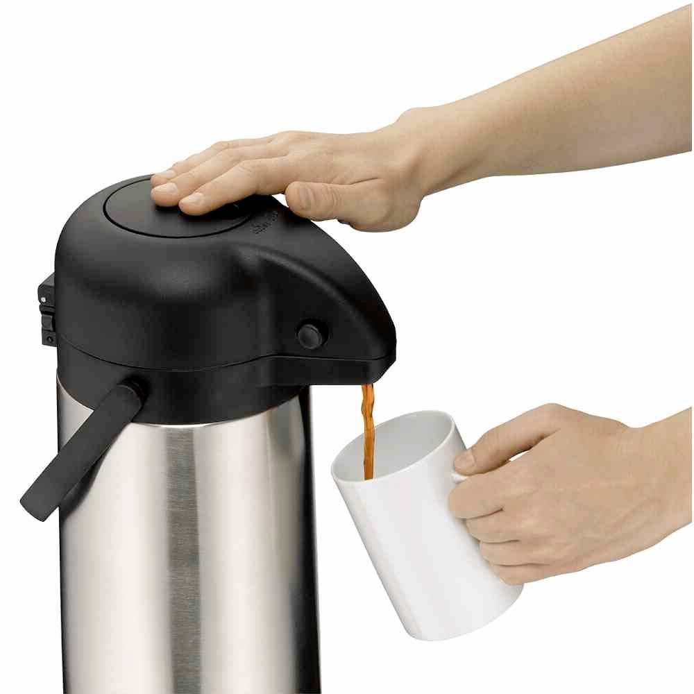 Une main appuie sur le levier d'un distributeur de thermos argenté, tandis qu'une autre main tient une tasse blanche en dessous, dans laquelle un liquide s'écoule.