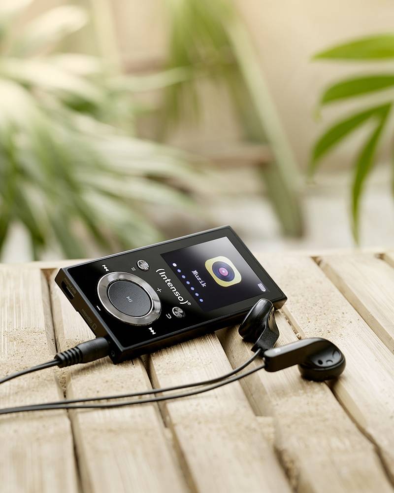 Un lecteur MP3 avec des écouteurs connectés est posé sur une table en bois. L'écran affiche une interface de lecture musicale.