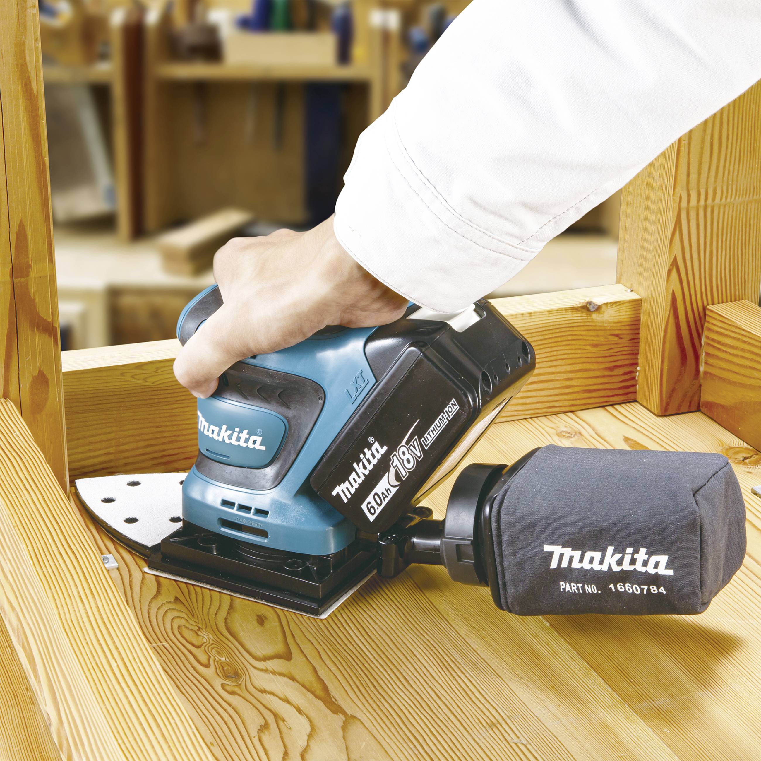 Un artisan utilise une meuleuse Makita bleue pour poncer une planche en bois. Des outils sont visibles en arrière-plan.