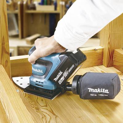 Un artisan utilise une meuleuse Makita bleue pour poncer une planche en bois. Des outils sont visibles en arrière-plan.