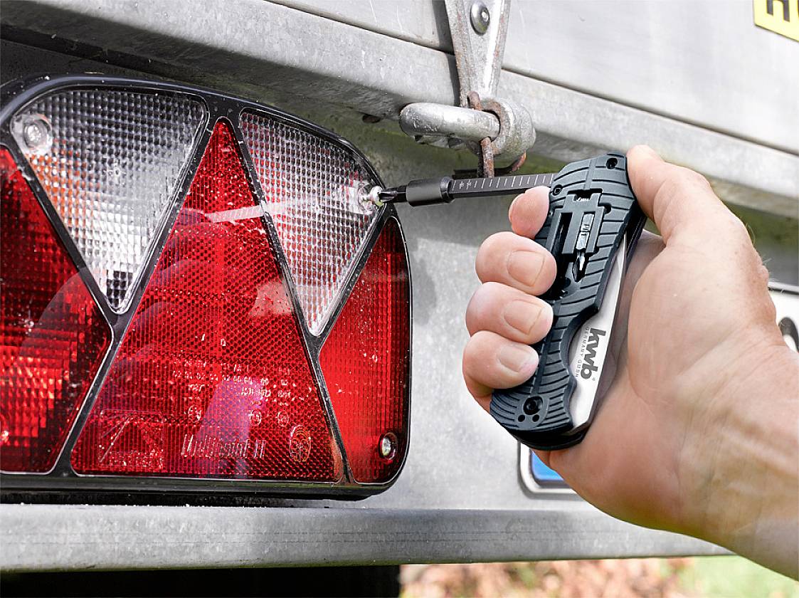 Une personne pulvérise de l'eau sur les feux arrière d'un véhicule à l'aide d'un appareil portable pour les nettoyer.