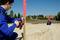 Deux personnes en tenue de travail bleue mesurent la distance entre un poteau en bois et un point au sol sur un chantier de construction à l'aide d'un mètre ruban.