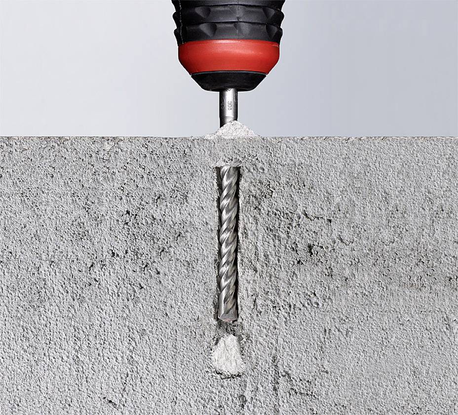 Un marteau-piqueur fore un trou dans du béton, avec de la poussière et des débris de béton visibles.