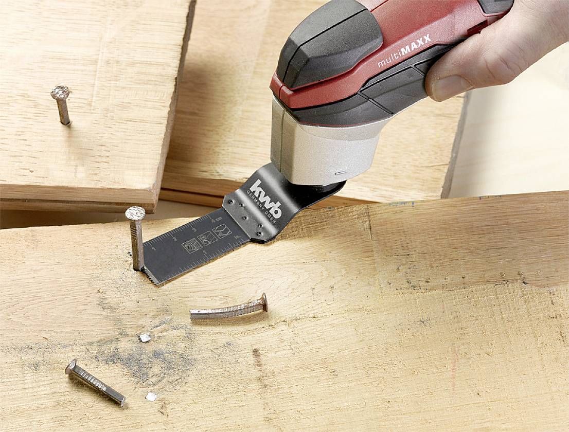 Une personne utilise un outil multifonction oscillant pour couper un clou dans une planche de bois.