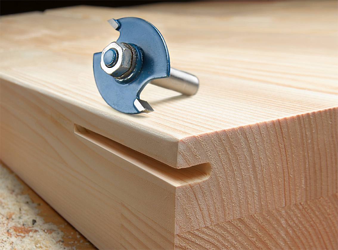 Fraise posée sur une table en bois avec son arête de fraisage ; utilisée pour couper des profils en bois.