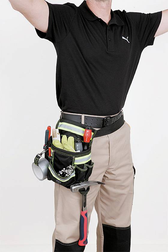 'Gros plan d'un artisan portant un pantalon beige et un polo noir, avec une ceinture à outils remplie d'instruments tels qu'un marteau et une pince.'