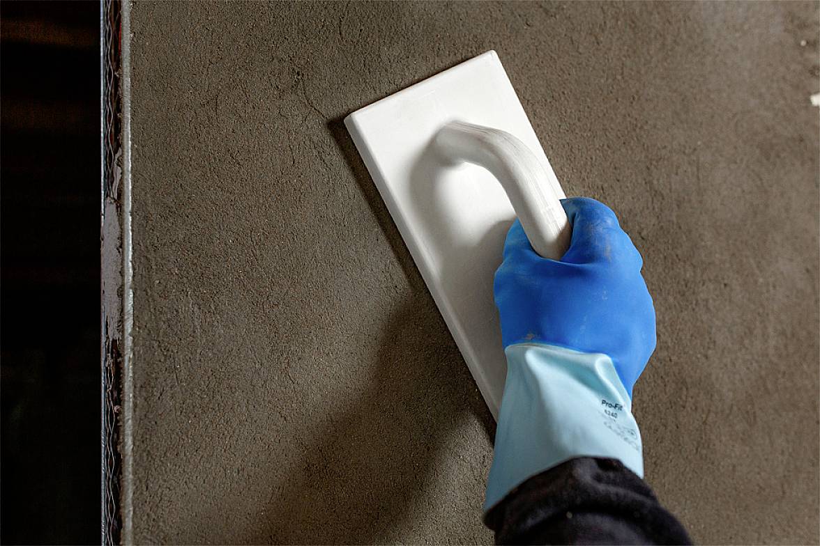 Une main gantée de bleu lisse un mur de béton avec une truelle.