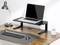 Un ordinateur portable est posé sur un support noir surélevé, sur une table en bois. À côté, une lampe de bureau et un clavier sont posés sur la table.