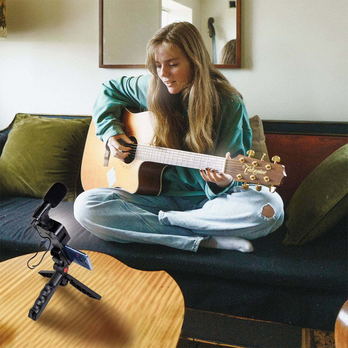 Une femme est assise sur un canapé et joue de la guitare. Devant elle, un microphone est posé sur une table, prêt à enregistrer.