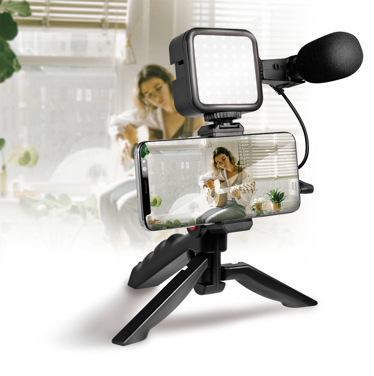 Un smartphone placé sur un trépied, avec un microphone et une lampe, montre une femme avec une guitare. Elle est également visible en arrière-plan.