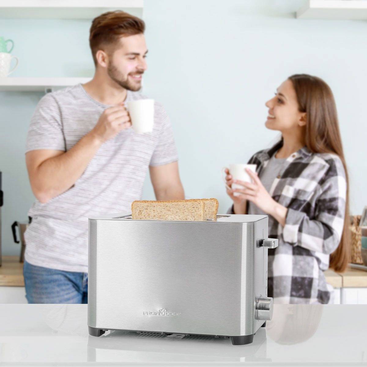 Un homme et une femme boivent du café dans la cuisine. Au premier plan, il y a un grille-pain avec des tranches de pain de mie.