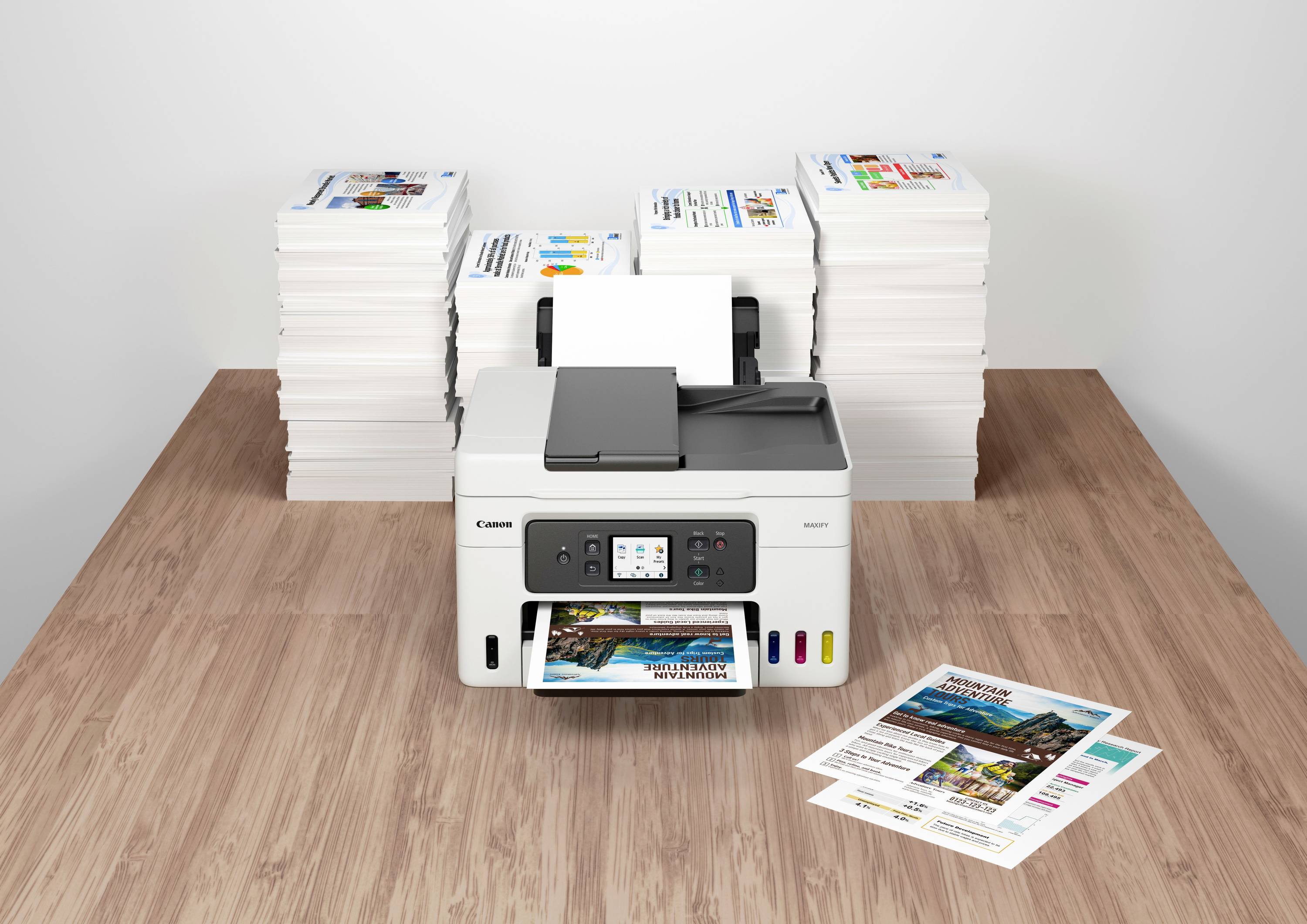 Une imprimante sur une table imprime des documents en couleur. À l'arrière-plan, des liasses de papier sont empilées.