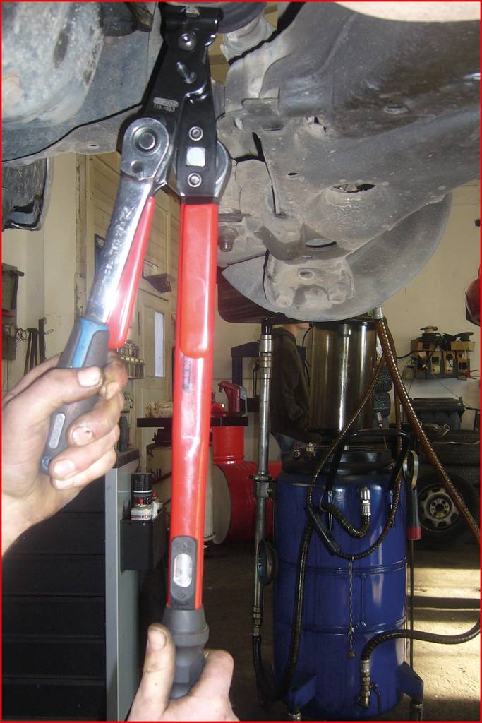 Une personne utilise un long levier rouge et une clé à molette pour travailler sur un véhicule surélevé.