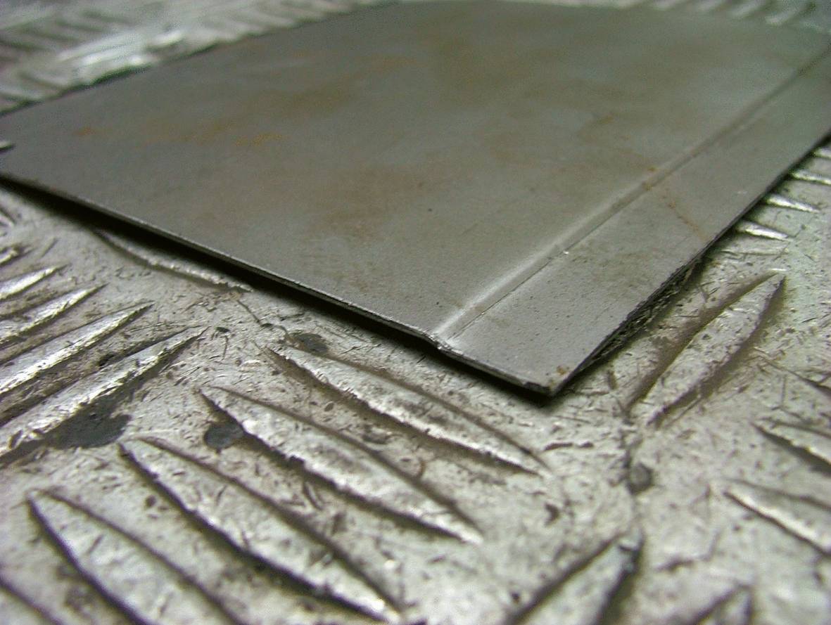 Une fine tôle métallique repose sur une surface métallique cannelée.
