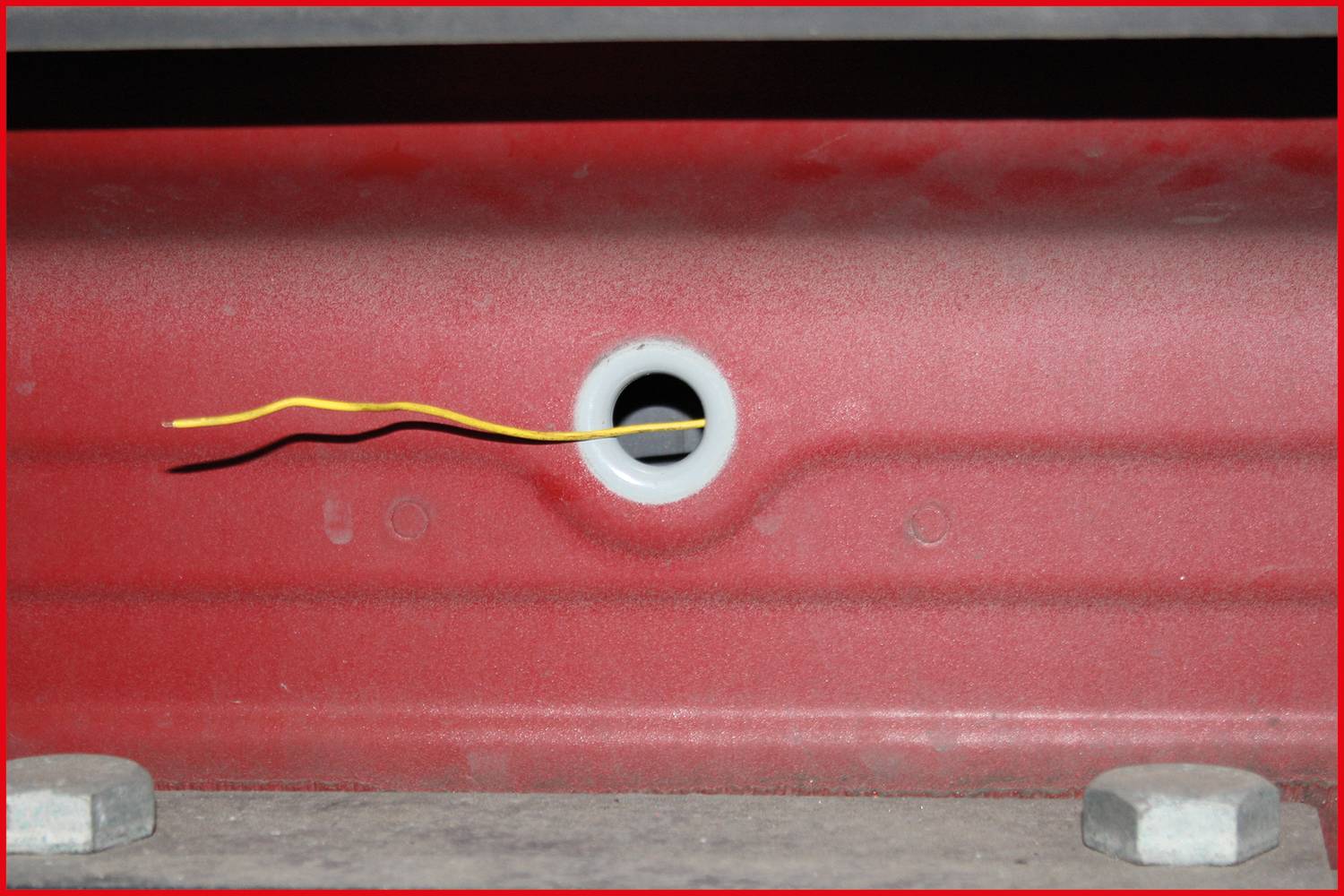 Une surface métallique rouge avec un petit trou au centre, d'où dépasse un câble jaune.