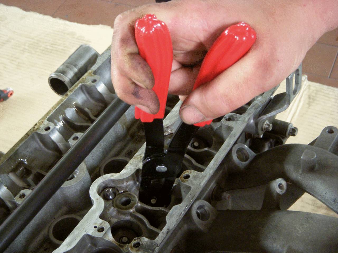 Une main utilise des outils de préhension rouges pour réparer ou ajuster des pièces dans un carter moteur ouvert.