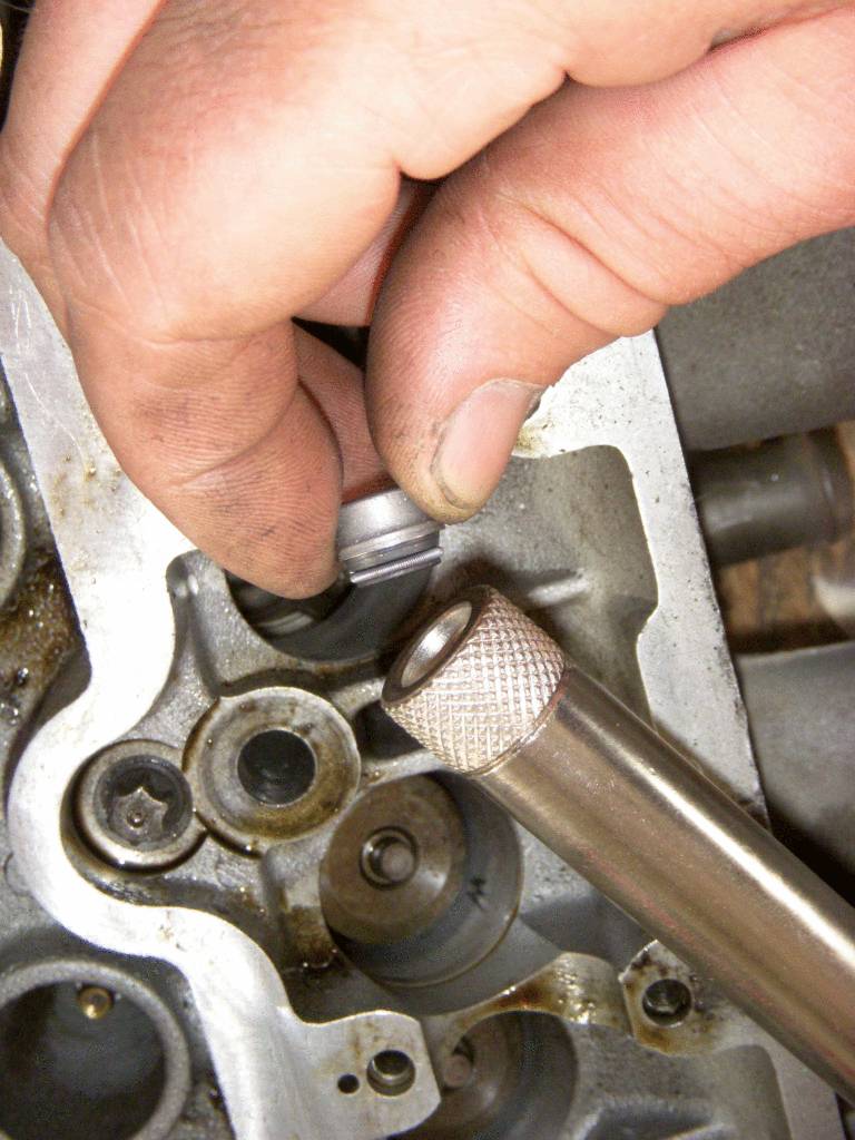 Une main monte un petit cylindre métallique dans un bloc-moteur.