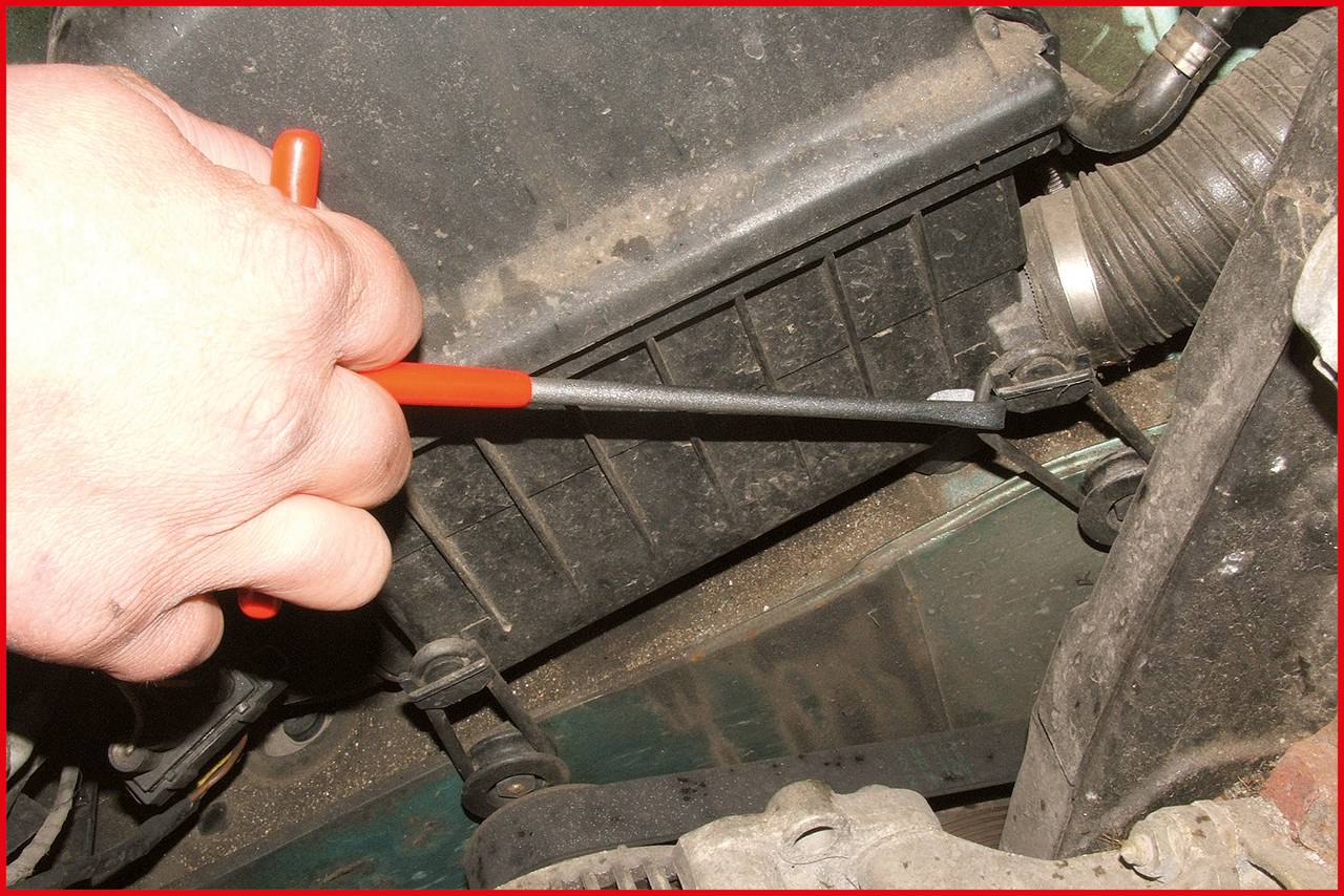 Une main utilise un tournevis pour ajuster les pièces d'un moteur. Des composants moteur sont visibles en arrière-plan.
