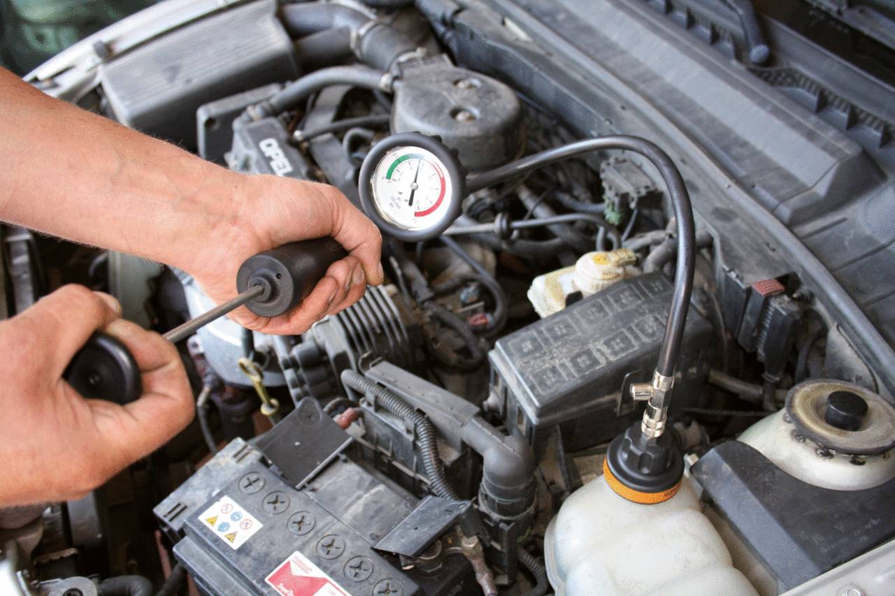 Une personne vérifie la pression d'un pneu de voiture avec un manomètre dans le compartiment moteur. Vue rapprochée des mains et de l'appareil de mesure.