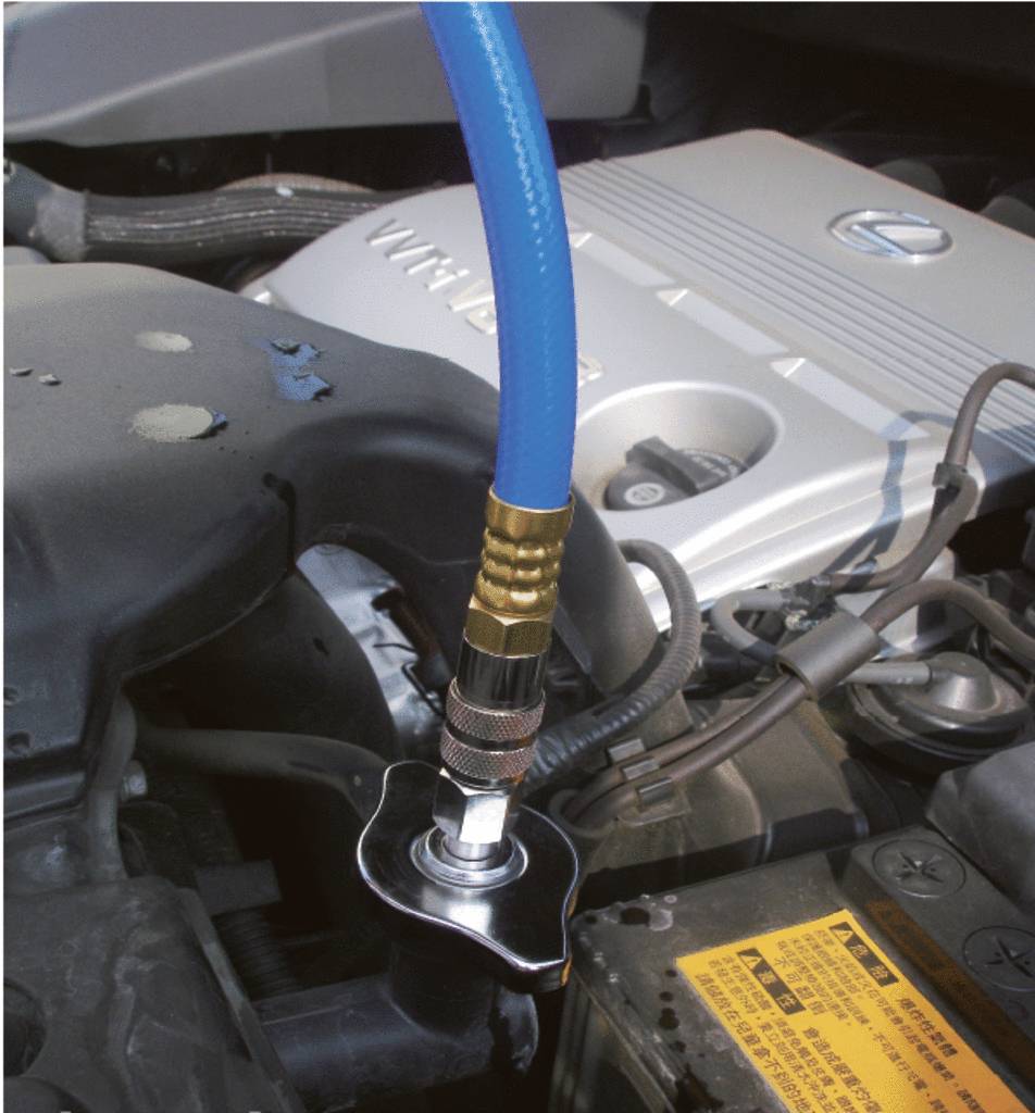 Un tuyau bleu est connecté au réservoir de liquide de refroidissement d'un compresseur automobile. L'arrière-plan montre des pièces de moteur.
