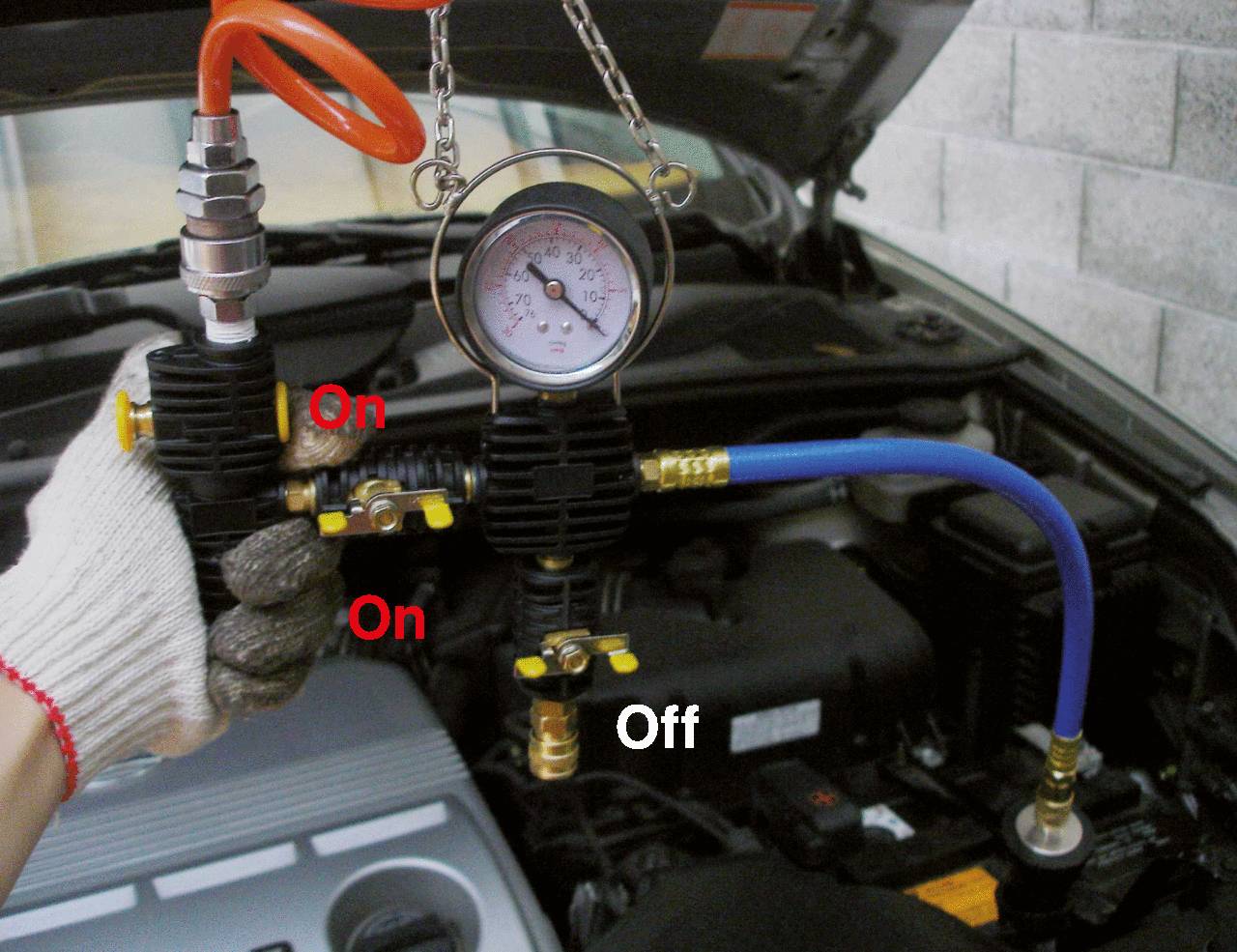 Un manomètre indique la pression dans un atelier automobile. Deux vannes sont marquées 'On', une vanne est marquée 'Off'. Le capot du moteur est ouvert.