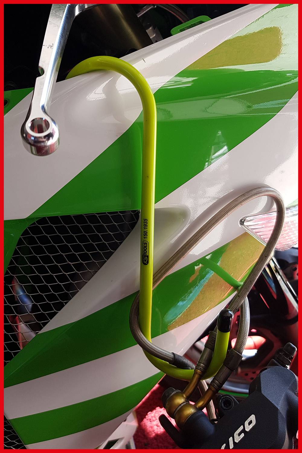 Moto avec un design de carénage vert et blanc. Un câble jaune est enroulé autour du guidon. Des outils sont visibles en arrière-plan.