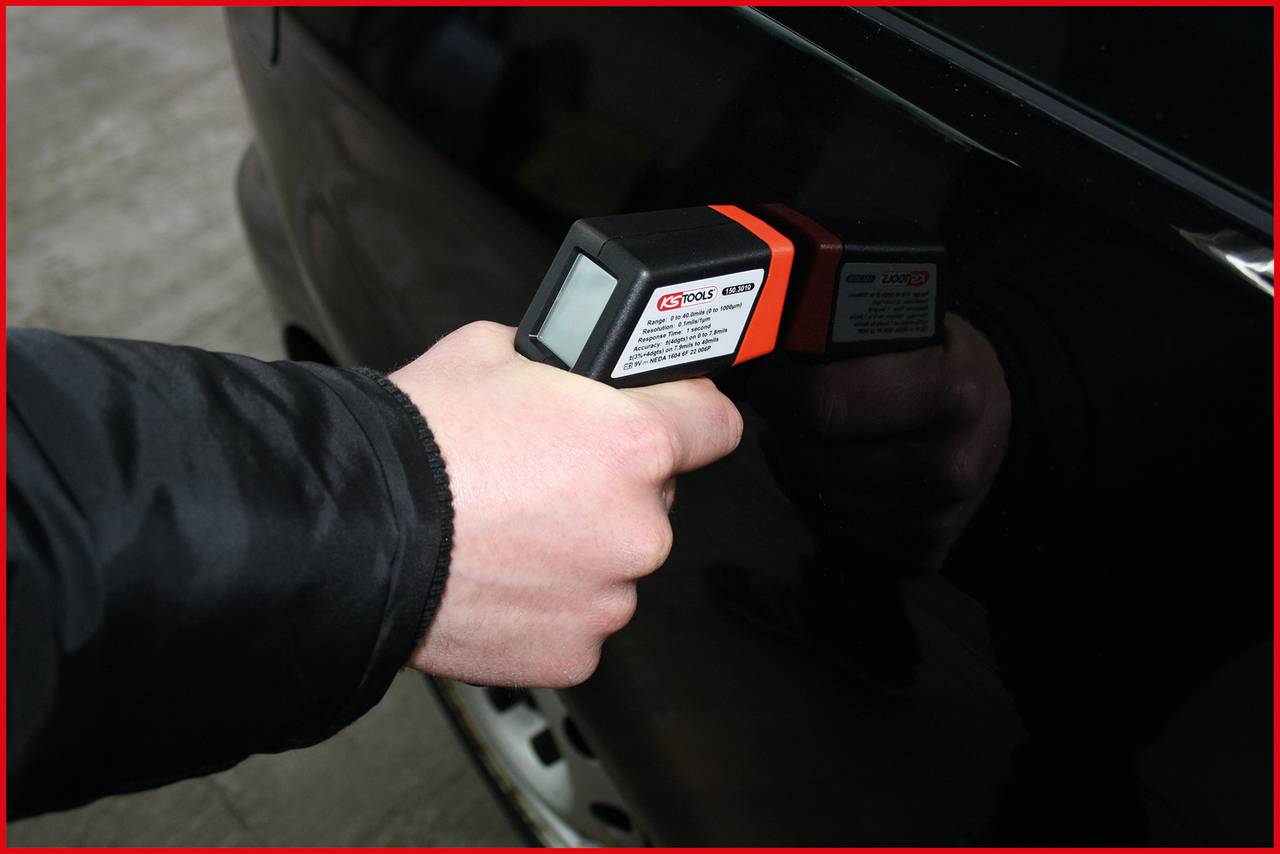 Une main tient un appareil portable contre la portière de voiture, qui semble être utilisé pour mesurer la température ou l'épaisseur.