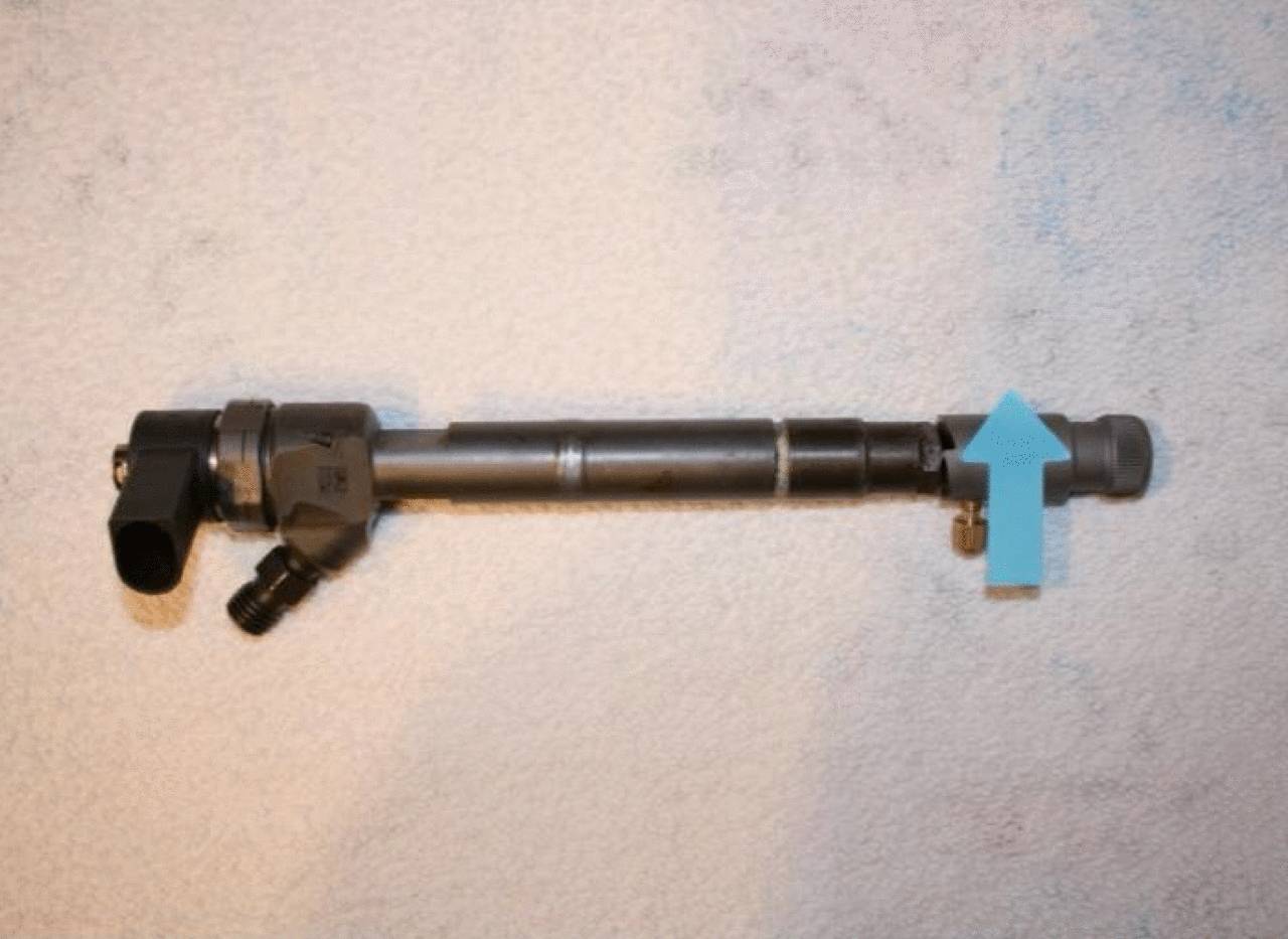 Un composant cylindrique noir avec une flèche bleue à droite. Il est posé sur un fond blanc.