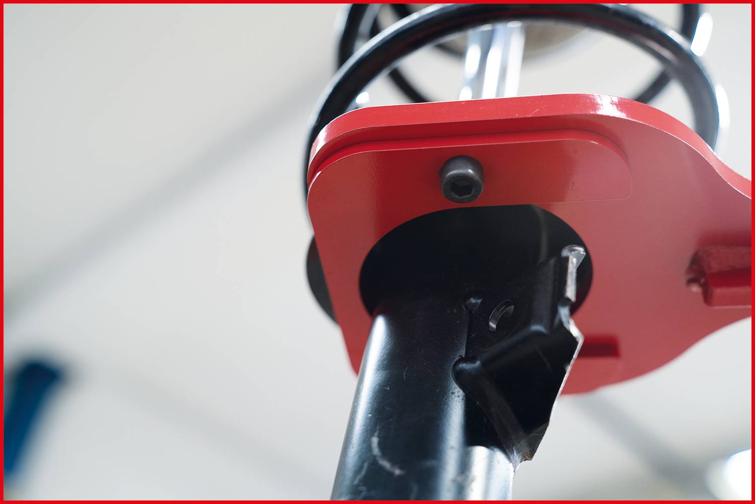 Gros plan d'une pièce métallique rouge fixée à une tige noire, probablement un composant d'une machine ou d'un équipement.
