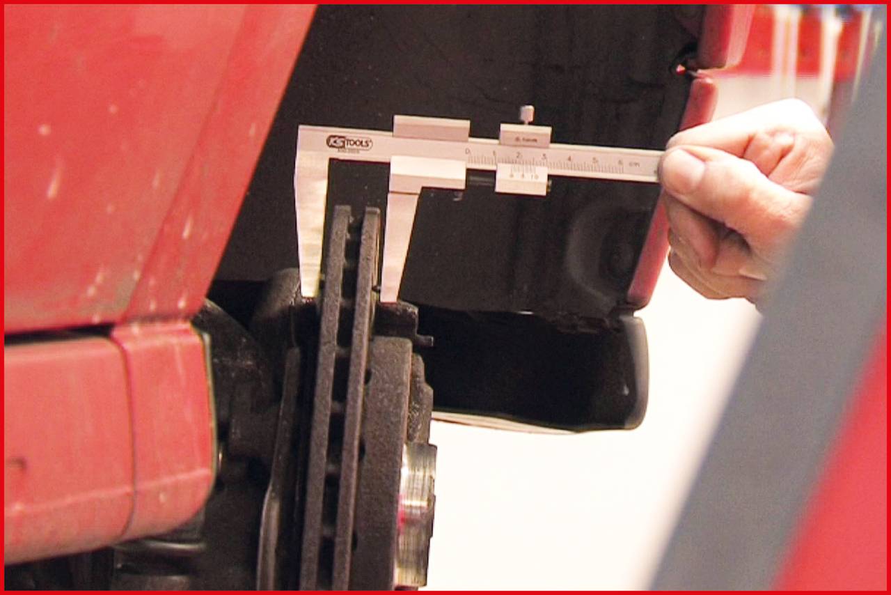 Quelqu'un mesure la distance sur une roue de véhicule à l'aide d'un pied à coulisse. L'accent est mis sur la mesure de précision dans un contexte technique.