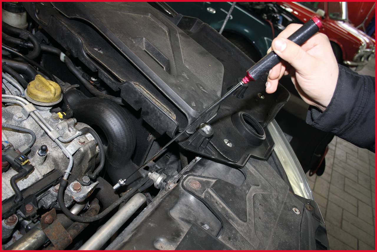 Une personne vérifie la jauge d'huile d'une voiture pour contrôler le niveau d'huile. Le compartiment moteur est visible en détail.