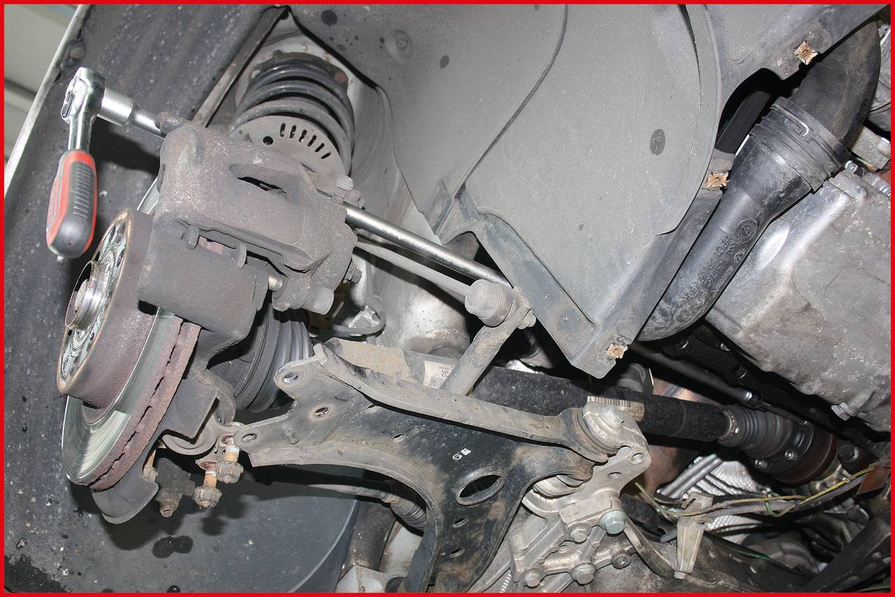 Une voiture est réparée par en dessous. On peut voir l'amortisseur avec une clé à molette travaillant sur la suspension.