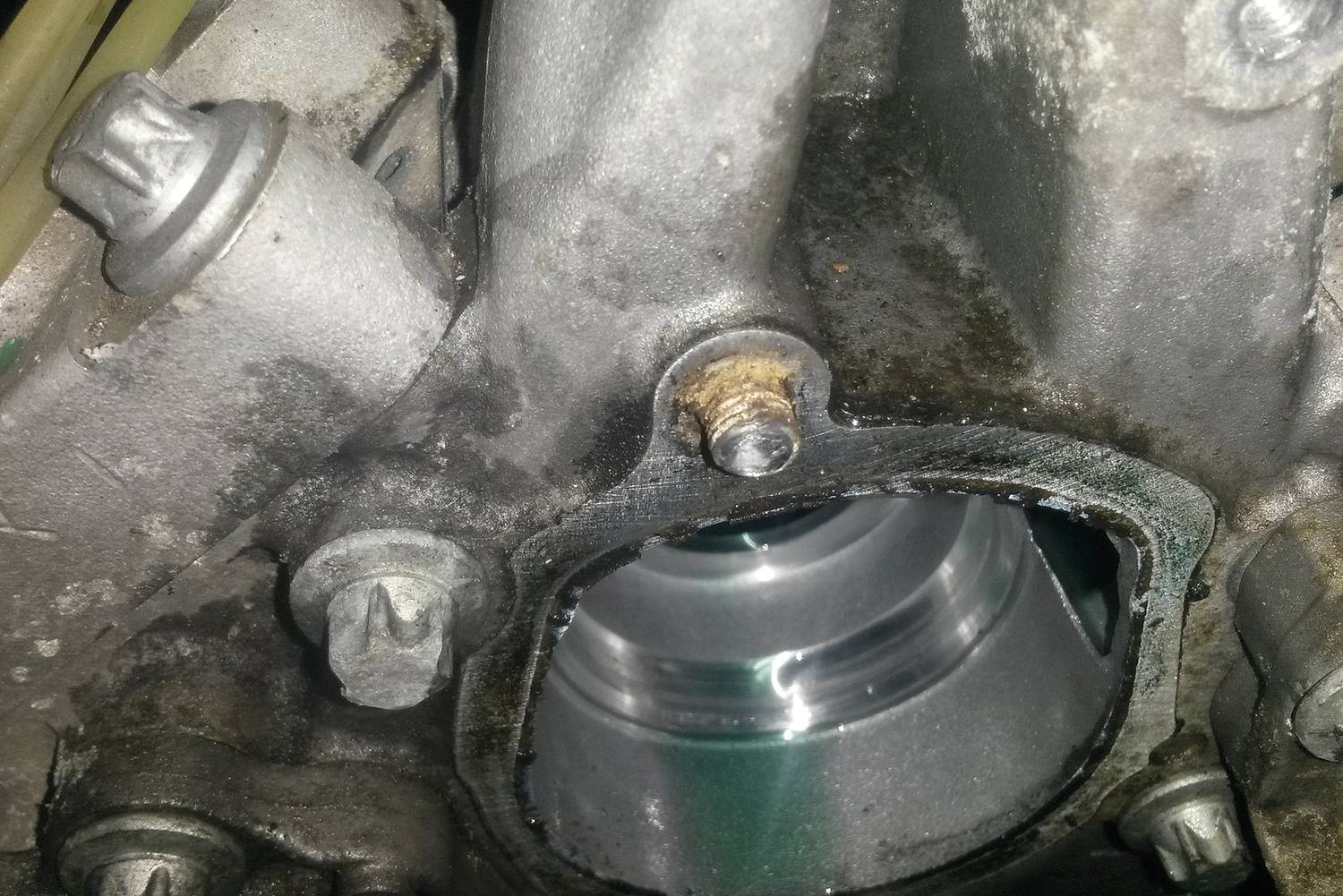 Gros plan sur un composant mécanique avec un boulon rouillé et une fuite d'huile visible, indiquant un besoin de maintenance.