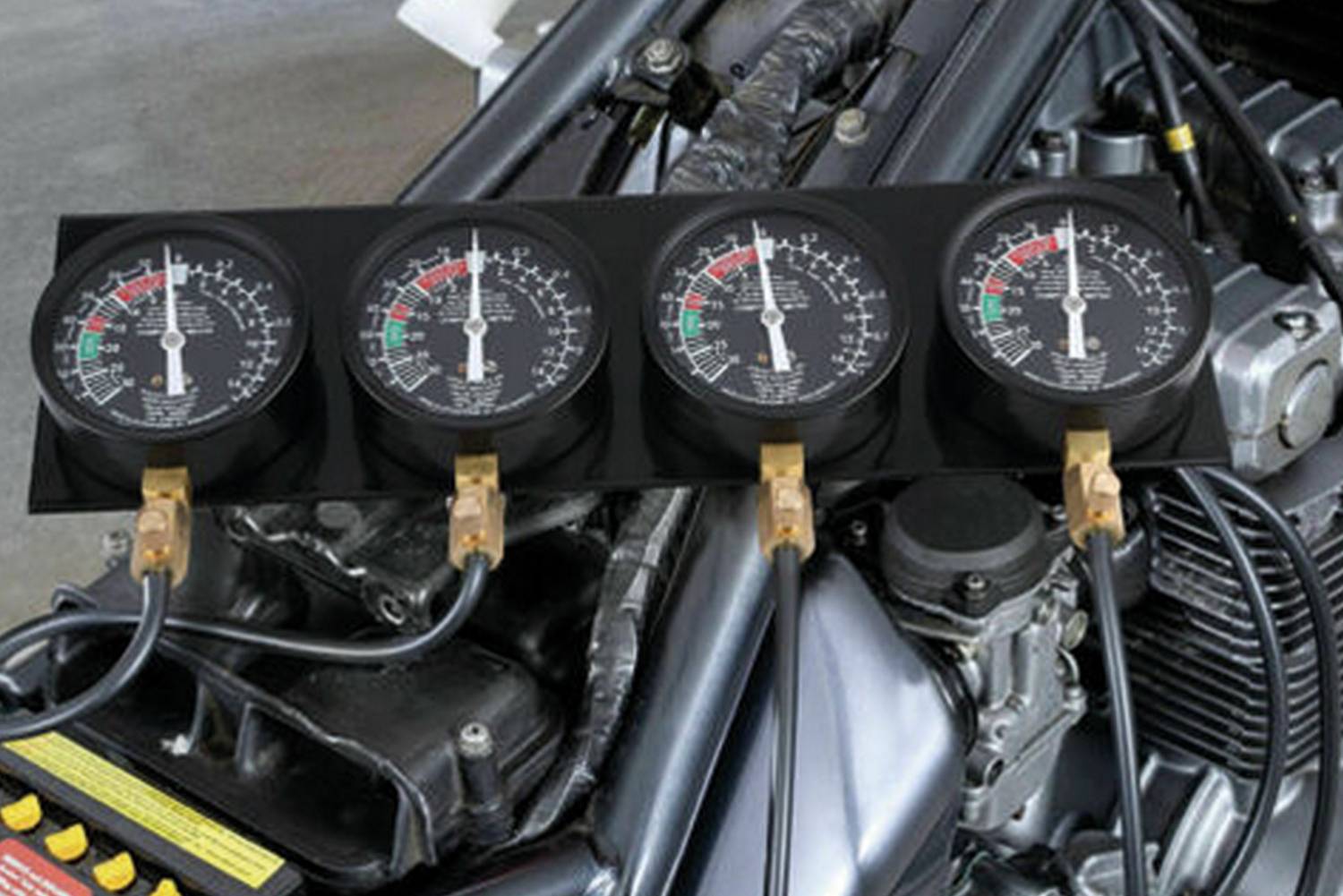 Quatre manomètres sont connectés à un moteur de motocyclette. Les affichages indiquent des valeurs de pression pour vérifier l'état du moteur.