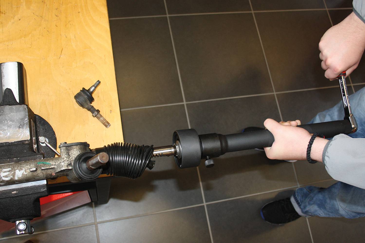 Une personne répare une pièce automobile dans un atelier. Un boîtier de direction est travaillé à l'aide d'une clé à molette.
