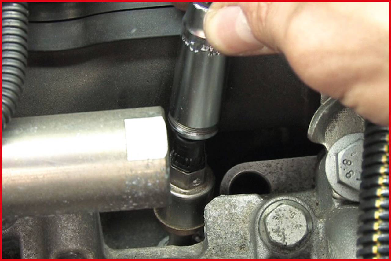 Une main change une bougie d'allumage sur le moteur d'une voiture. Une clé à molette est utilisée pour retirer ou serrer la bougie.