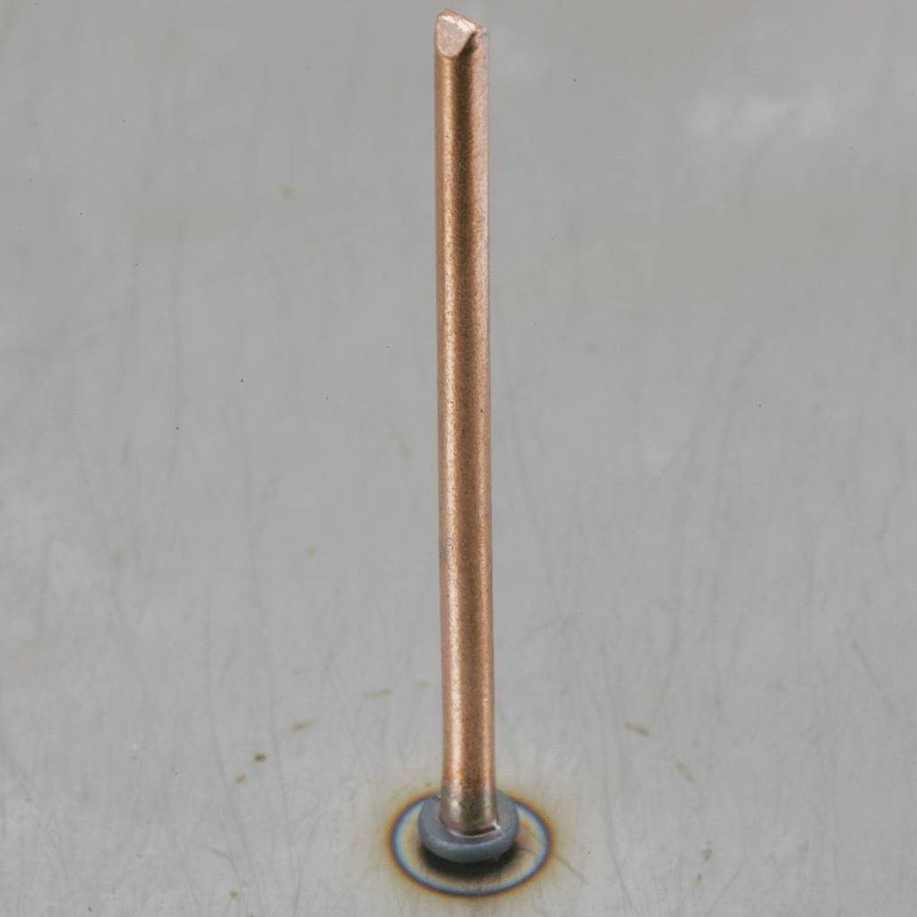 Un unique barreau de cuivre se dresse verticalement sur une surface métallique grise. Sa partie supérieure est coupée à plat.