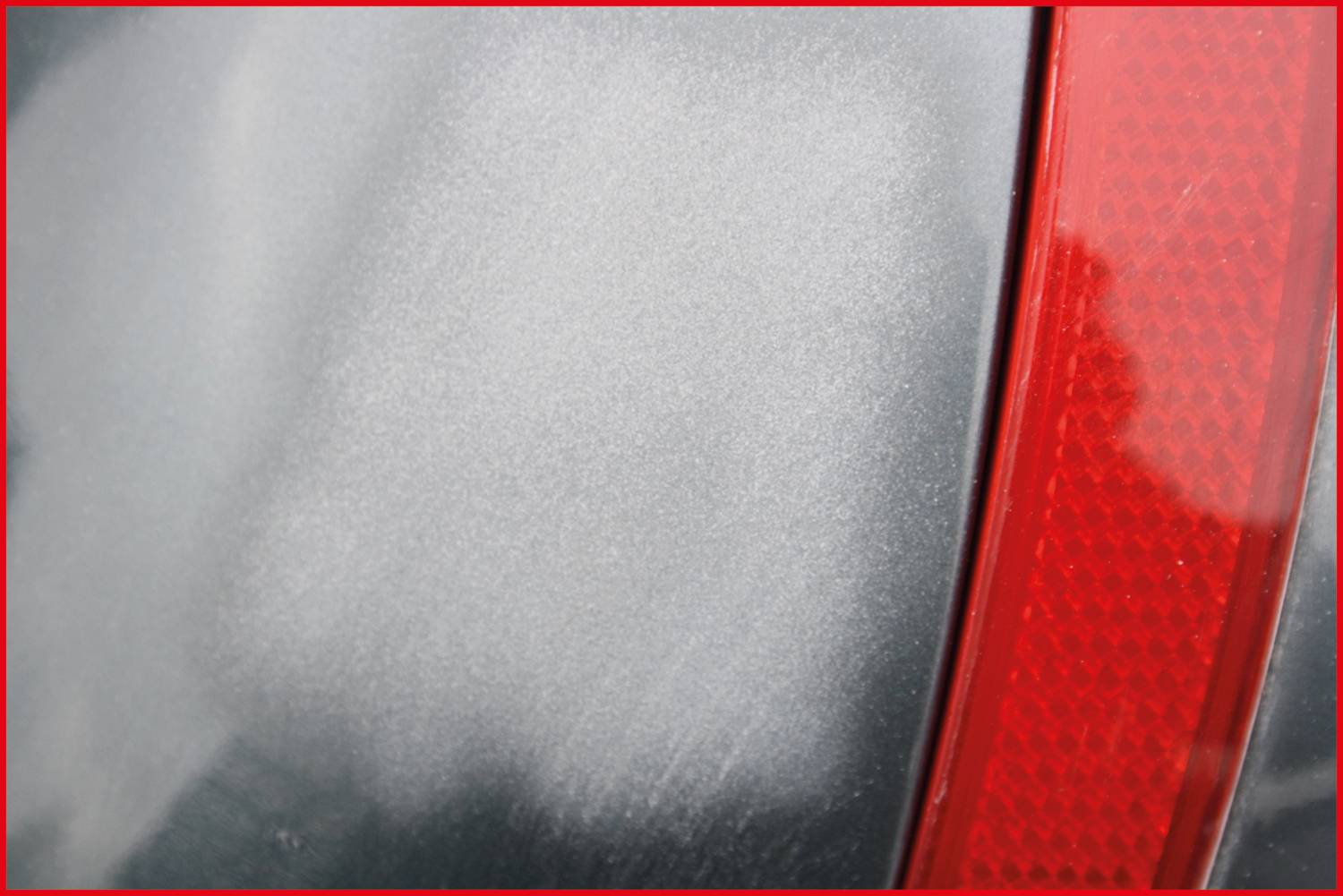 Gros plan sur la peinture d'une voiture avec un feu arrière rouge. La surface présente quelques légères rayures, témoignant d'une usure.