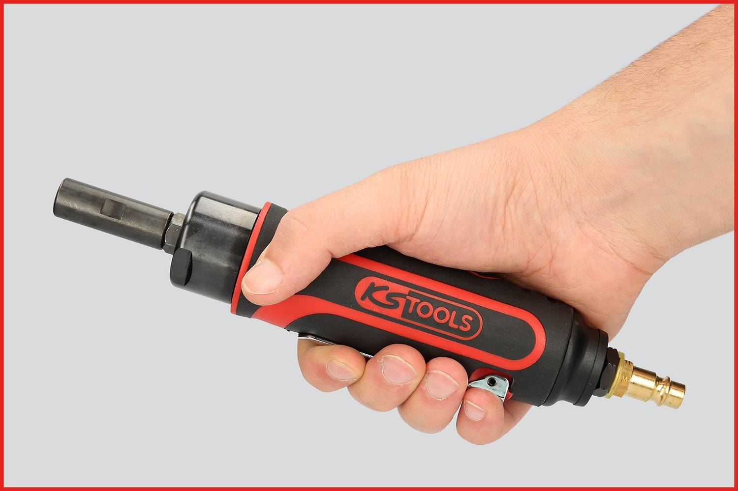 Une main tient un mini-amoleur pneumatique de KS Tools, de couleur rouge et noir, avec un raccord en laiton, devant un fond gris.
