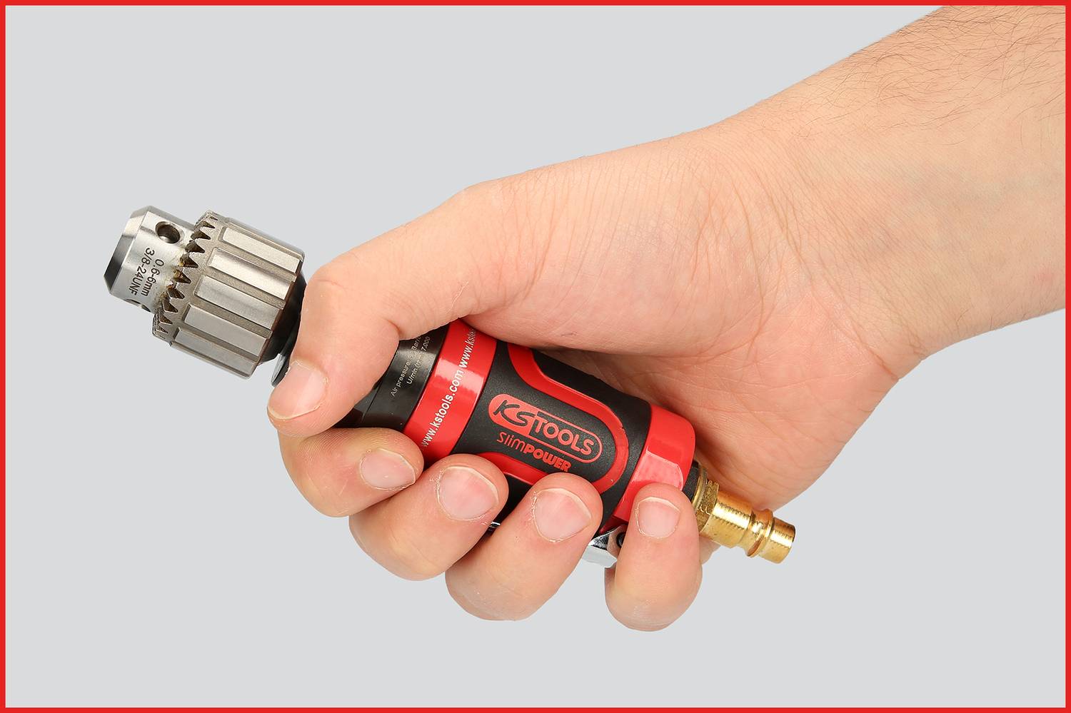 Une personne tient un outil rouge et noir avec un mandrin de perceuse. L'outil semble conçu pour des travaux manuels.