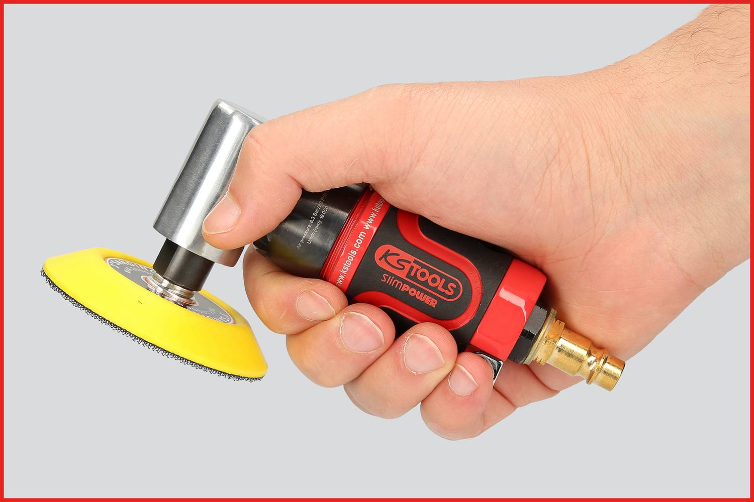 Une main tient un outil pneumatique rouge et noir avec un embout de polissage jaune. L'outil est prêt à être utilisé.