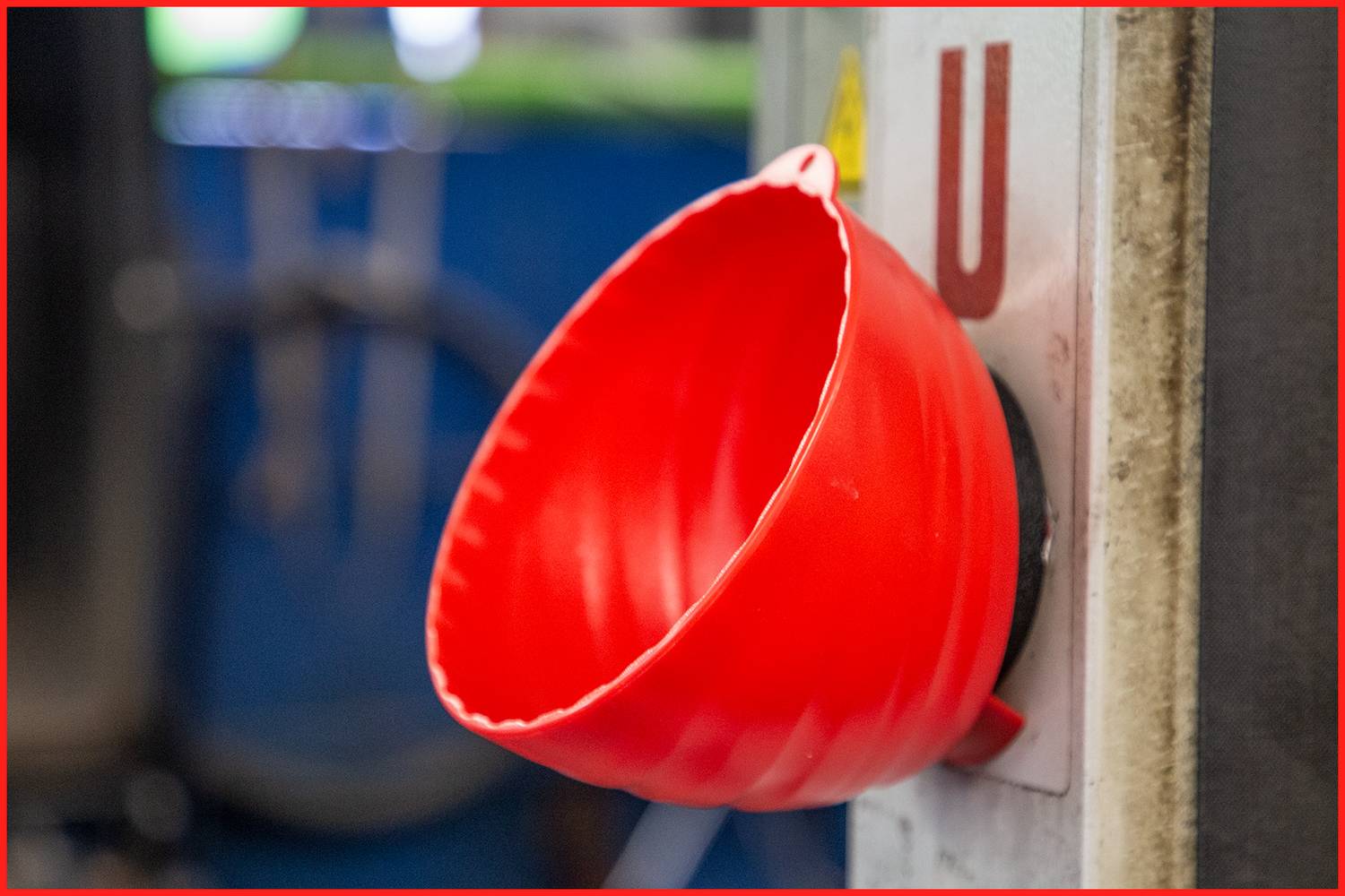 Couvercle de protection rouge sur un interrupteur ou une vanne, probablement pour la sécurité ou pour empêcher la manipulation. Arrière-plan flou.