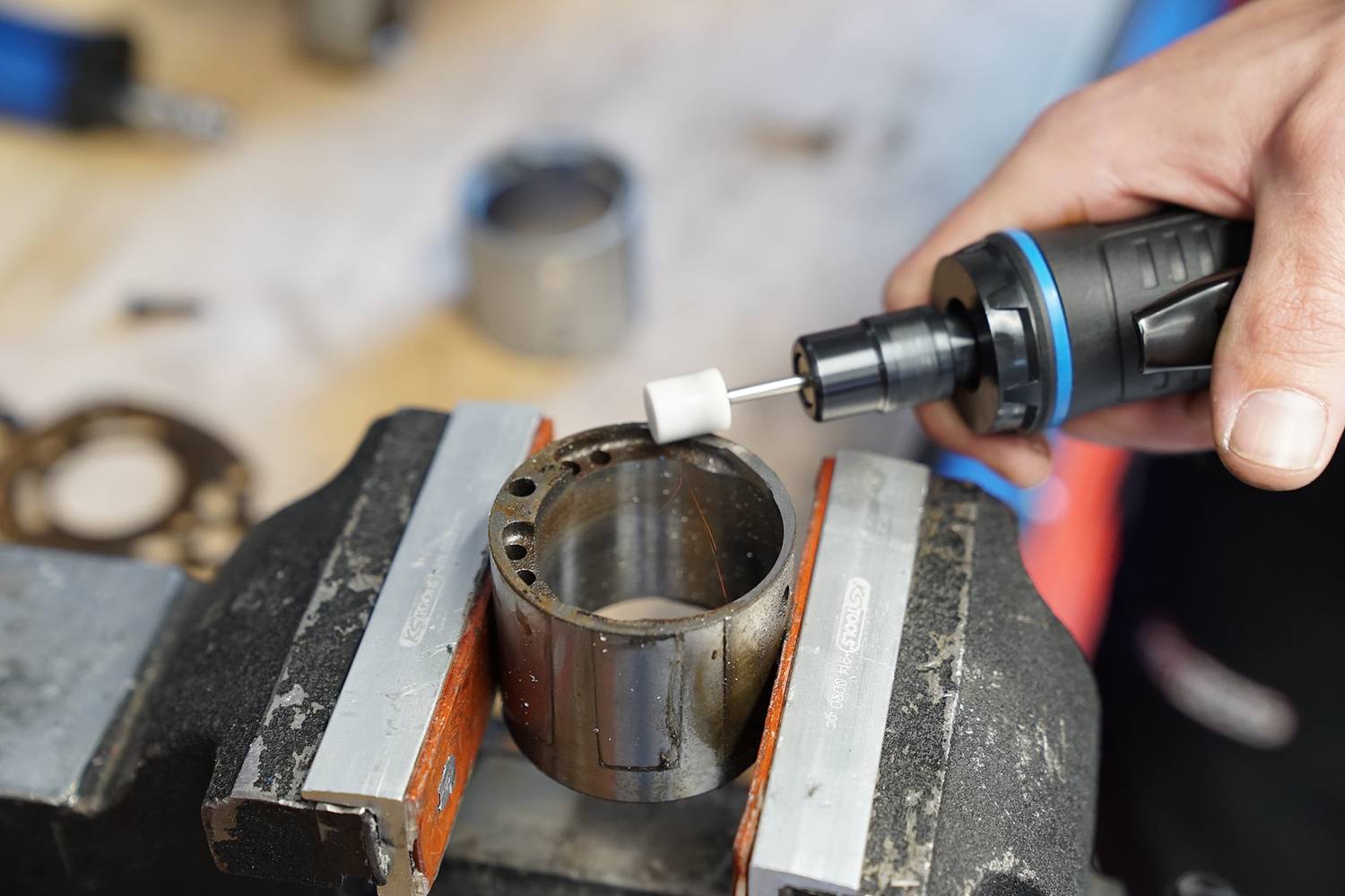 Gros plan d'une personne travaillant une pièce métallique dans un étau à l'aide d'un outil rotatif. Des outils en arrière-plan sont flous.