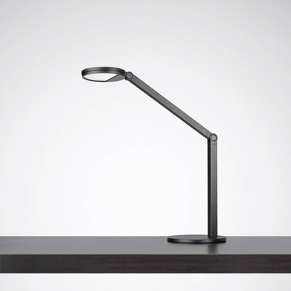 Une lampe de table moderne noire avec un bras articulé, posée sur une table en bois sombre.