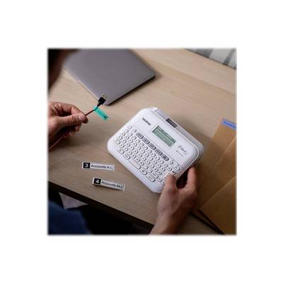 Une personne travaille avec une imprimante d'étiquettes et étiquette des câbles USB. Un ordinateur portable et des enveloppes sont posés sur la table.