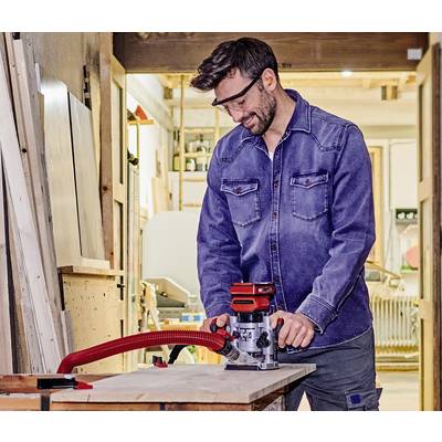 Un homme en tenue de travail utilise une fraiseuse à bois dans un atelier. Portant des lunettes de protection, il se concentre sur la planche de bois.