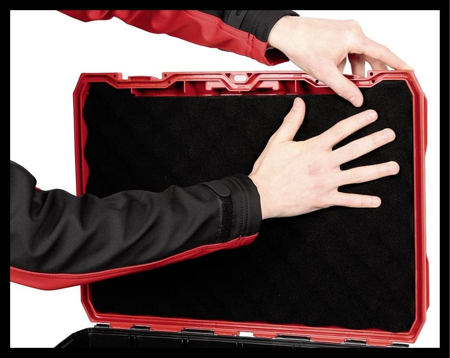 Une personne place un insert en mousse noir dans une valise rouge. Des mains positionnent soigneusement l'insert.